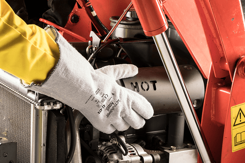 Worker wearing ActivArmr® 42-474 mechanical gloves repairs a hot machine part, ensuring safety and precision in a high-temperature setting