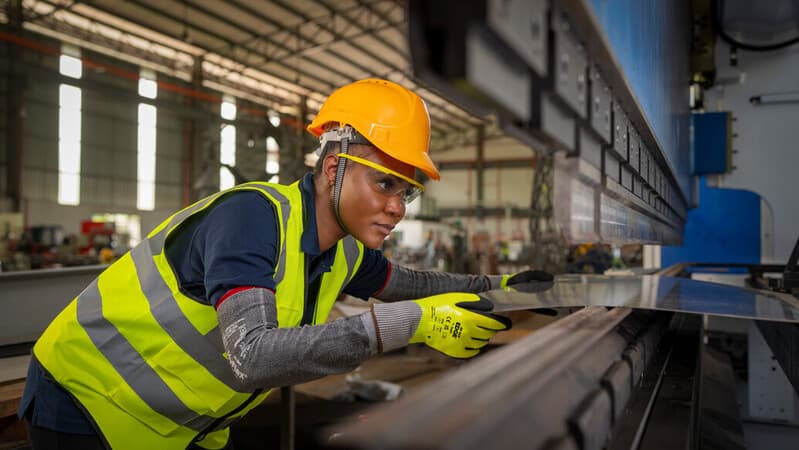 Worker wearing EDGE 48-969 mechanical gloves handles metal sheets with precision and care