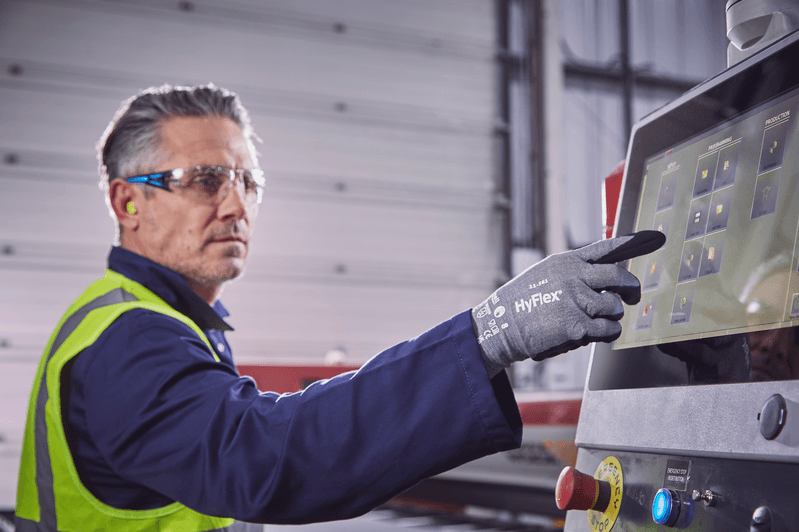 Worker wearing HyFlex® 11-581 mechanical gloves operates a computer to review tool settings, ensuring safety and efficient adjustments