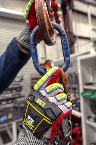 Hand wearing R-065 mechanical glove holding a large metal chain link in an industrial setting