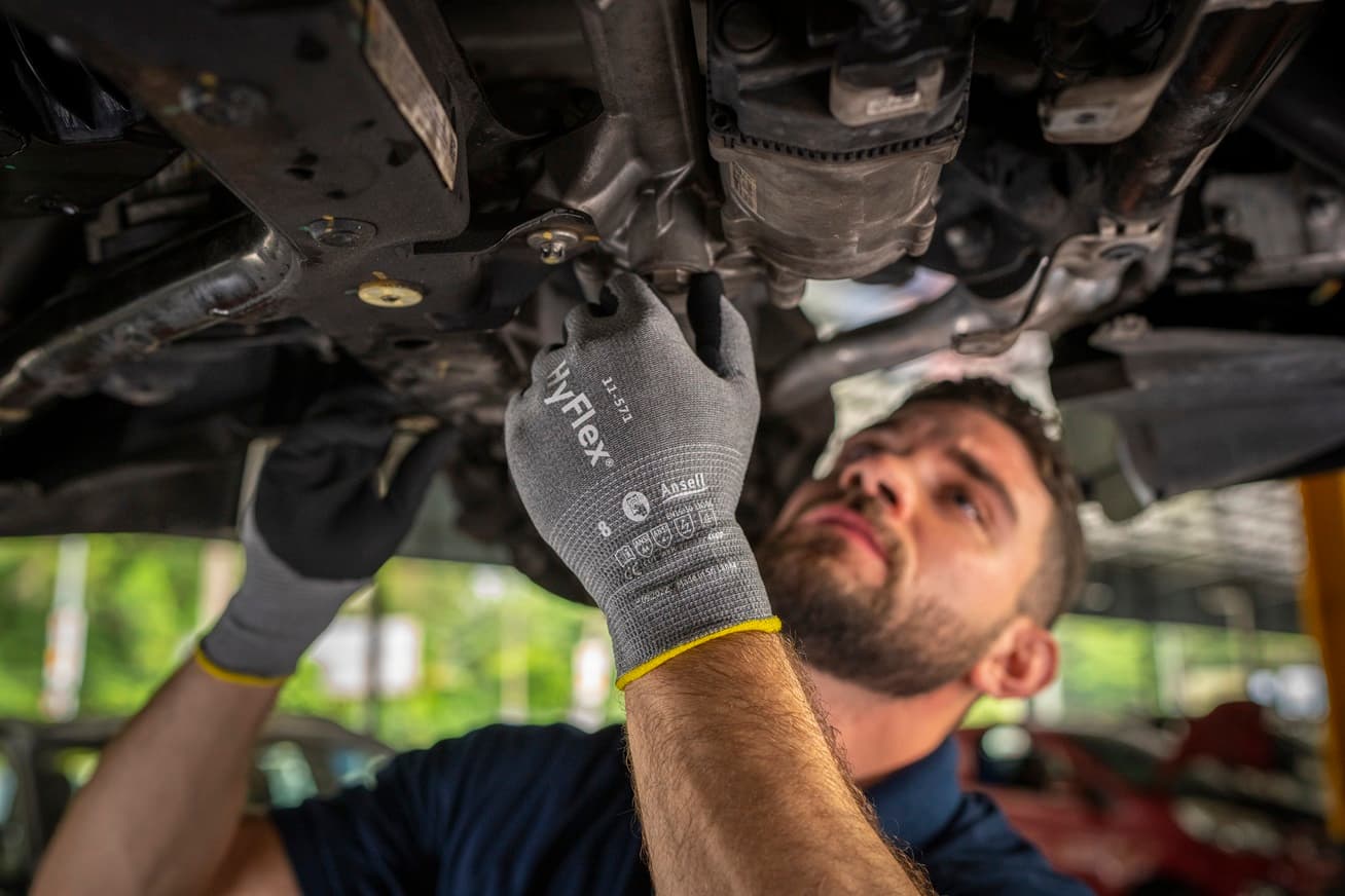 A worker adjusts an engine wearing HyFlex® 11-571 mechanical gloves, ensuring precision and safety in a repair setting.