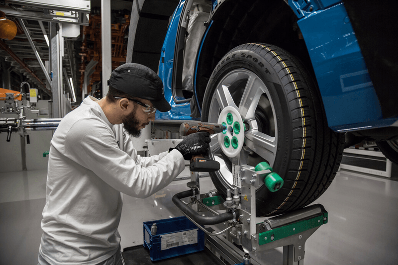 Worker wearing HyFlex® 11-591 mechanical gloves assembles car parts, ensuring safety and precision in the automotive assembly process.