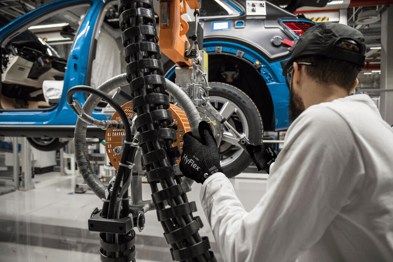 Worker wearing HyFlex® 11-591 mechanical gloves assembles car parts, ensuring safety and precision in the automotive assembly process.