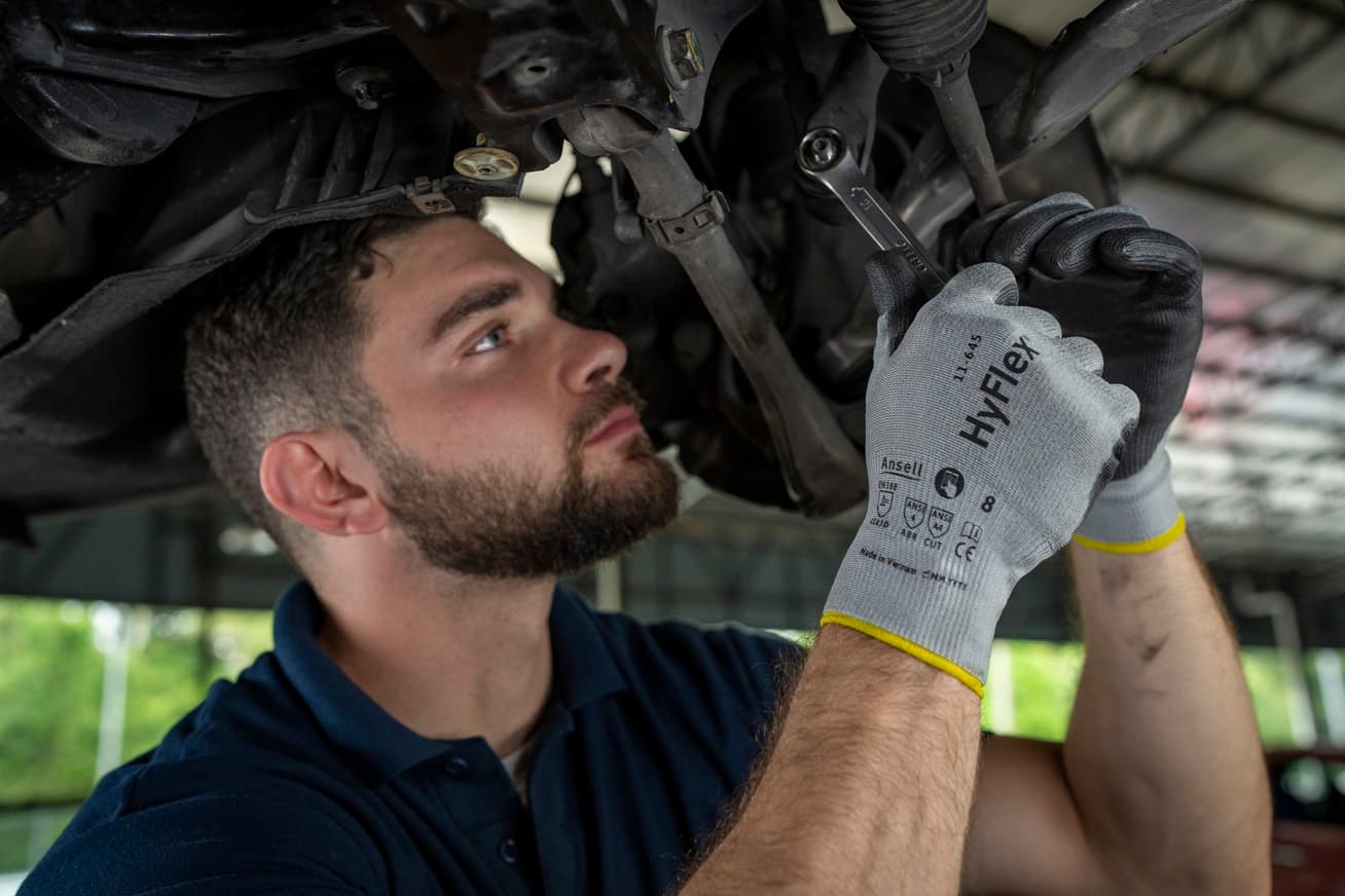 Worker adjusts car engine with HyFlex® 11-645 mechanical gloves, ensuring precision and safety in a repair setting