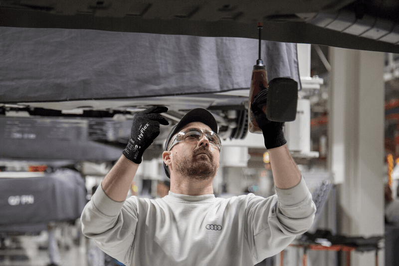 Worker wearing HyFlex® 11-591 mechanical gloves assembles car parts, ensuring safety and precision in the automotive assembly process.