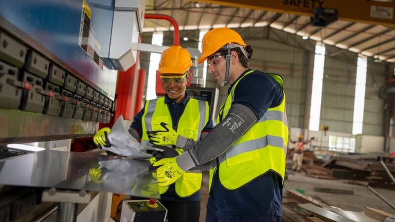 Worker wearing EDGE 48-969 mechanical gloves handles metal sheets with precision and care