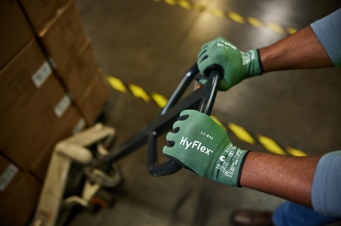Worker wearing HyFlex® 11-842 mechanical gloves moves boxes in a warehouse, ensuring grip and protection during lifting tasks.