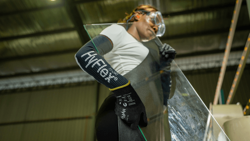 Worker carefully handles a large glass sheet in a manufacturing facility wearing HyFlex® 11-543 mechanical gloves