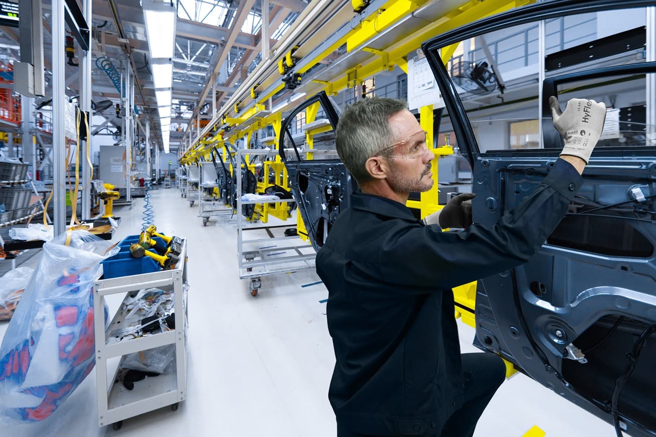 Worker wearing HyFlex® 11-645 mechanical gloves assembles car parts, ensuring safety and precision in the automotive assembly process.
