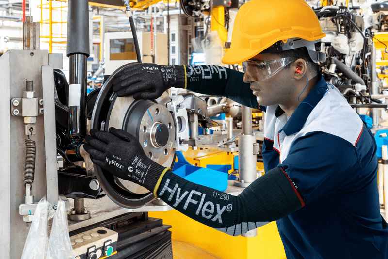 Worker wearing HyFlex® 11-543 mechanical gloves assembles car parts, ensuring safety and precision in the automotive assembly process.
