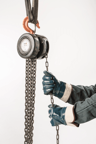 Worker wearing ActivArmr® Hycron® 27-805 protective mechanical gloves operates a heavy-duty chain hoist, pulling the chain to lift or lower a load