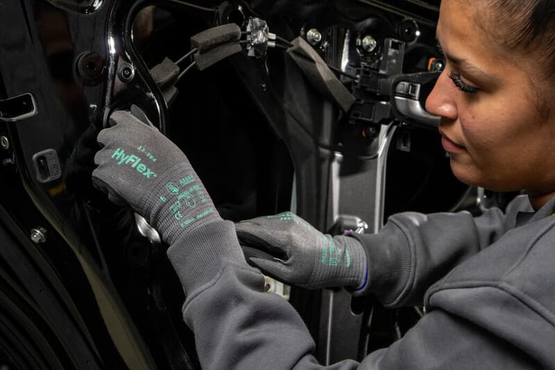Worker assembling automotive parts with tools while wearing HyFlex 11-584 gloves for cut protection.
