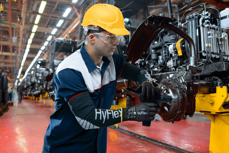 Worker wearing HyFlex® 11-543 mechanical gloves assembles car parts, ensuring safety and precision in the automotive assembly process.